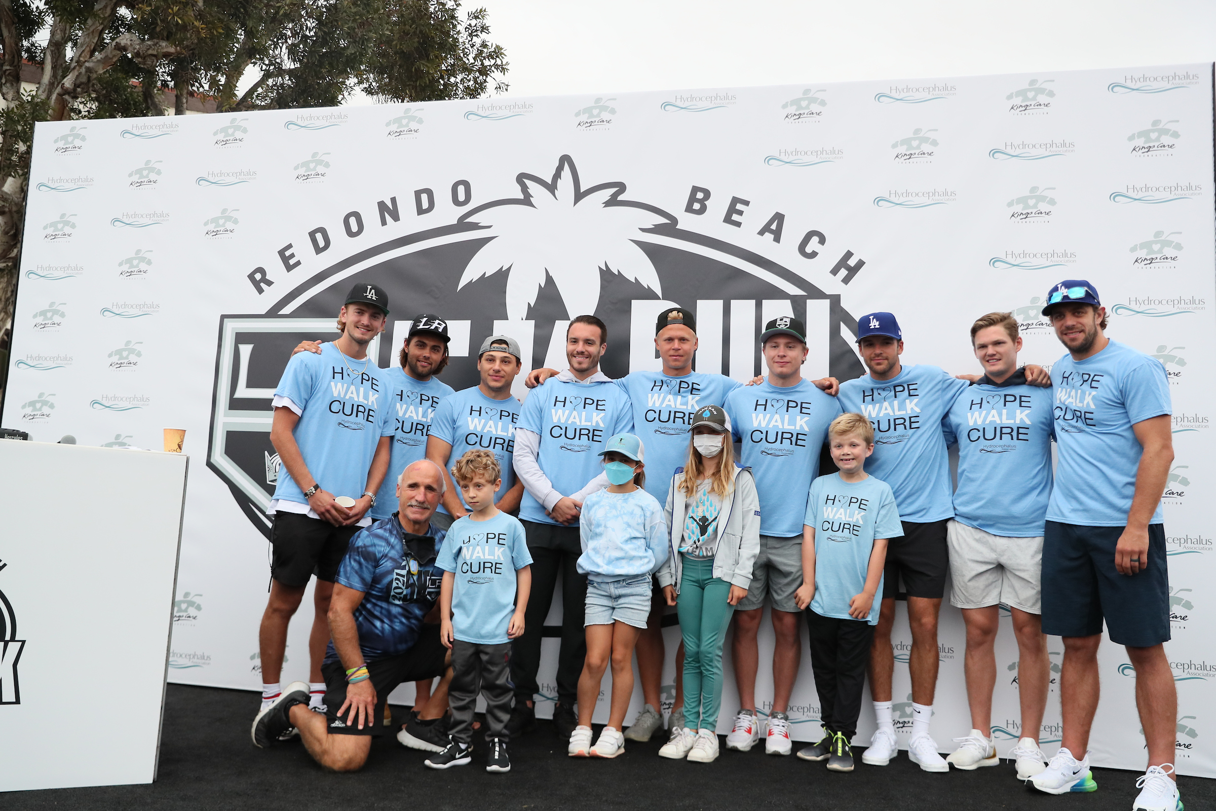 LA Kings players in blue shirts stand in a line with children in front of them for a photo at the LA Kings 5K.
