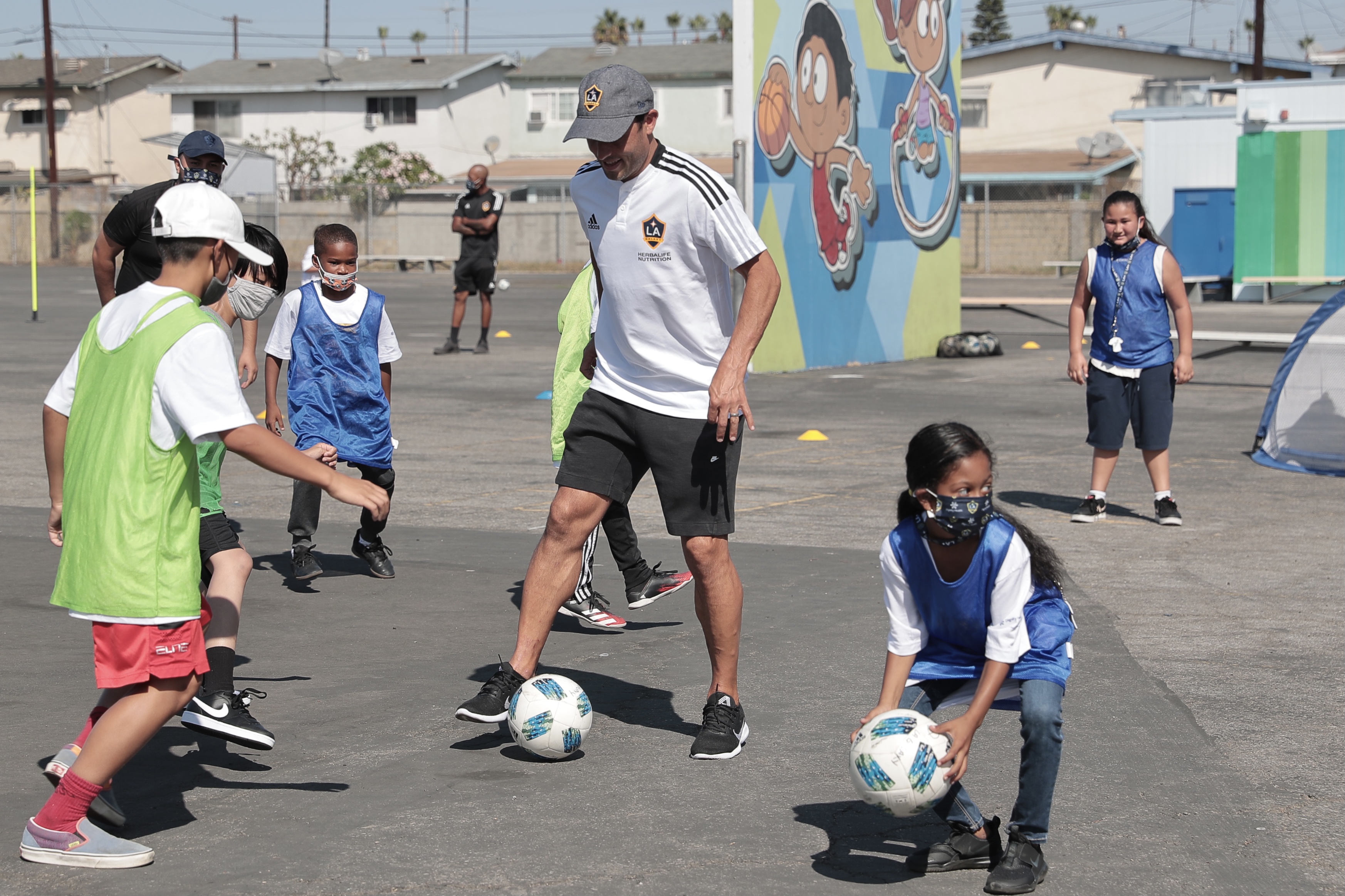 Landon Donovan kicks a soccer ball around with local elementary school students in Carson, CA. 