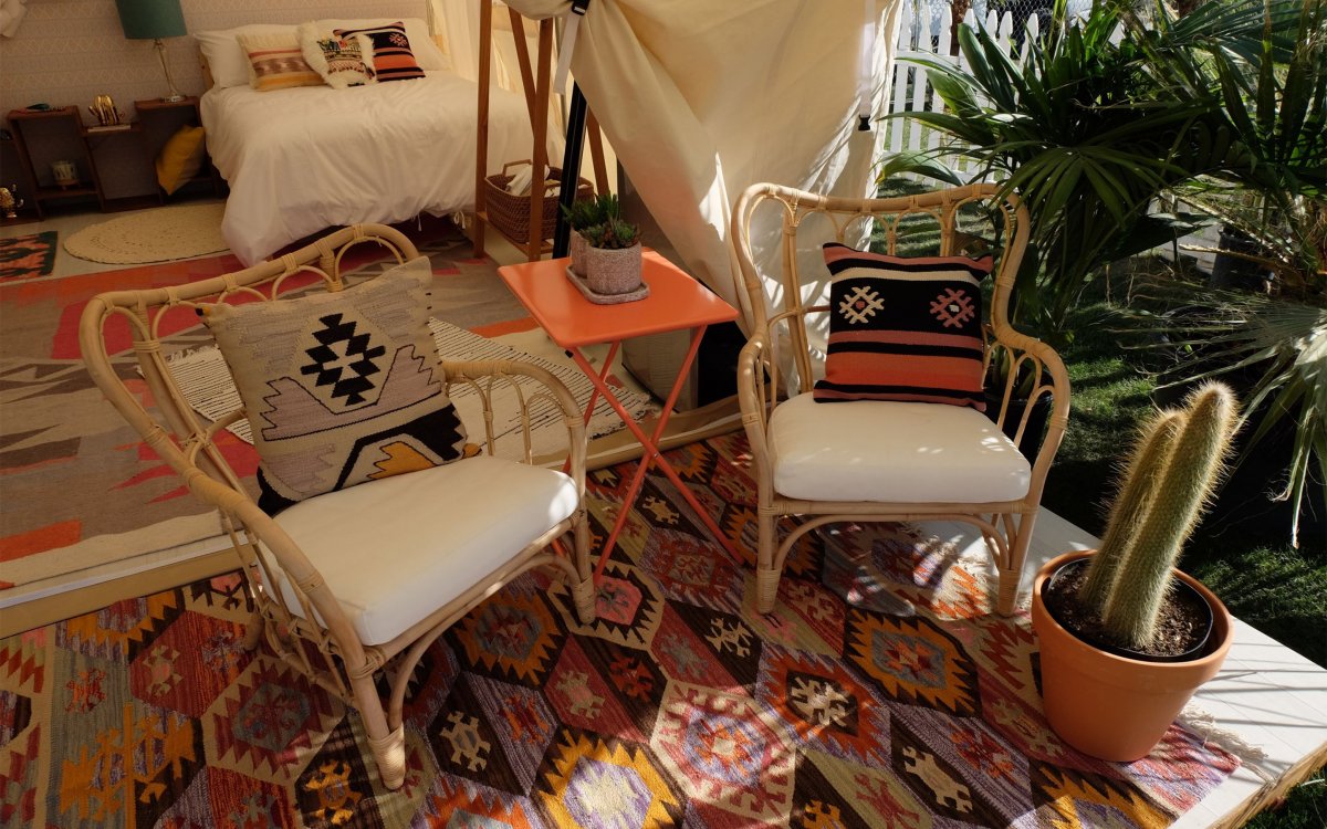 Image of two chairs with a bed in the background decorated in tribal print under a tent similar to a teepee