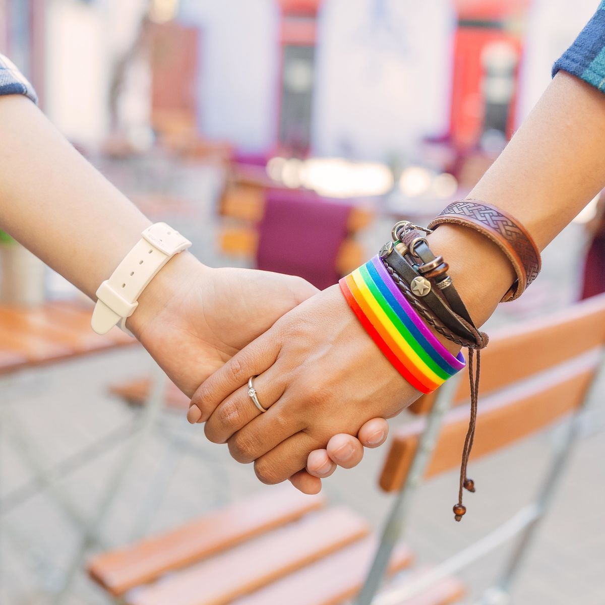 Two women hold hands - one wearing a Pride rainbow bracelet. 