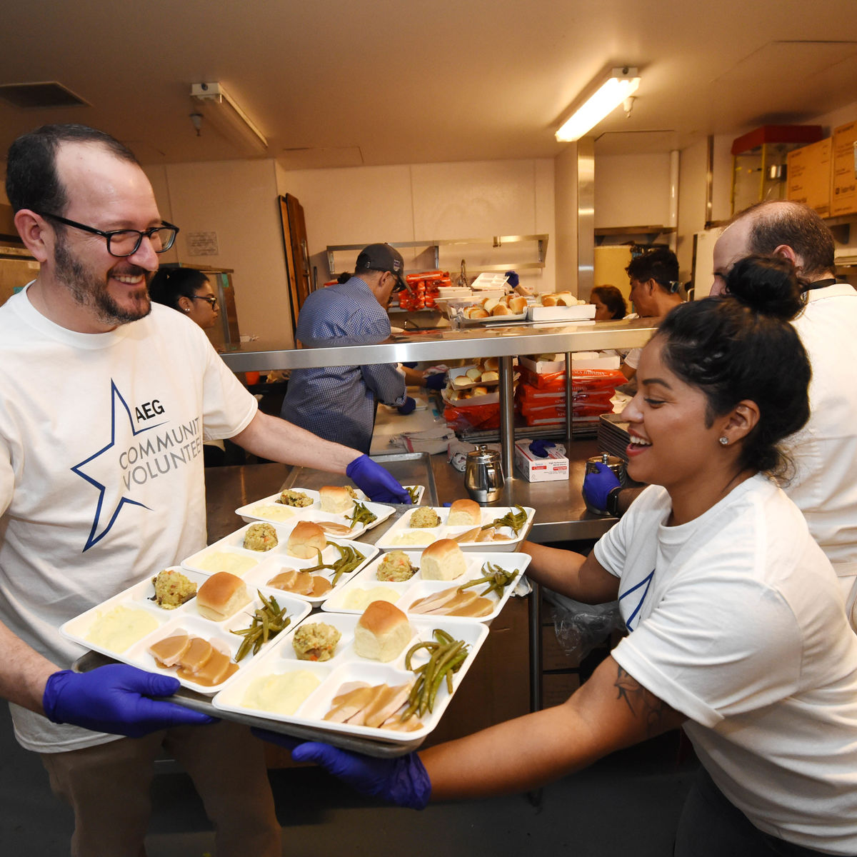 AEG CEO & President Dan Beckerman hands a tray of prepared Thanksgiving meals to another volunteer in the kitchen at The Novo at L.A. LIVE. 