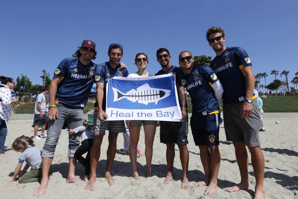 Galaxy players and volunteers holding a flag that says "Heal The Bay" on the beach