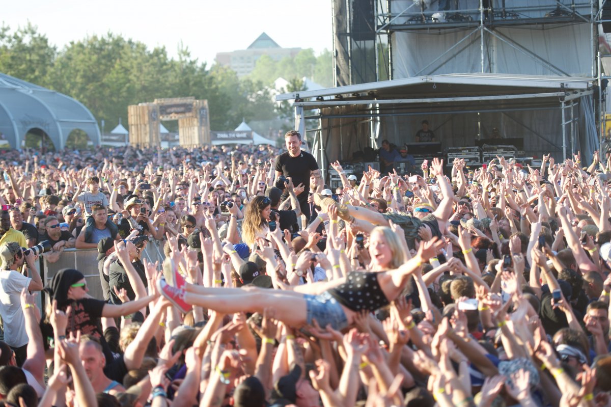 Image of a crowd with two people crowd surfing and a performer standing above the crowd
