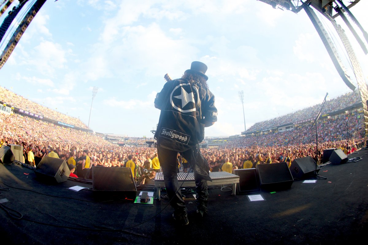 Image of the back of a performer playing the guitar to a crowd during the day at Rock on the Range