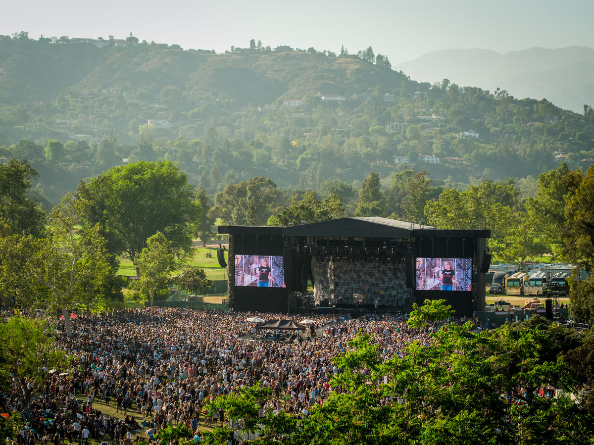 Image of stage and crowd from a distance with trees and hills in background