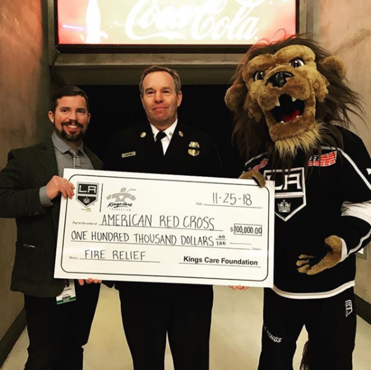AEG Sports COO Kelly Cheeseman, Chief Deputy Fred Mathis – the Commander of LA City Fire Department’s Administrative Operations Bureau – and LA Kings mascot Bailey hold a $100,000 check for the American Red Cross to be used toward fire relief efforts.