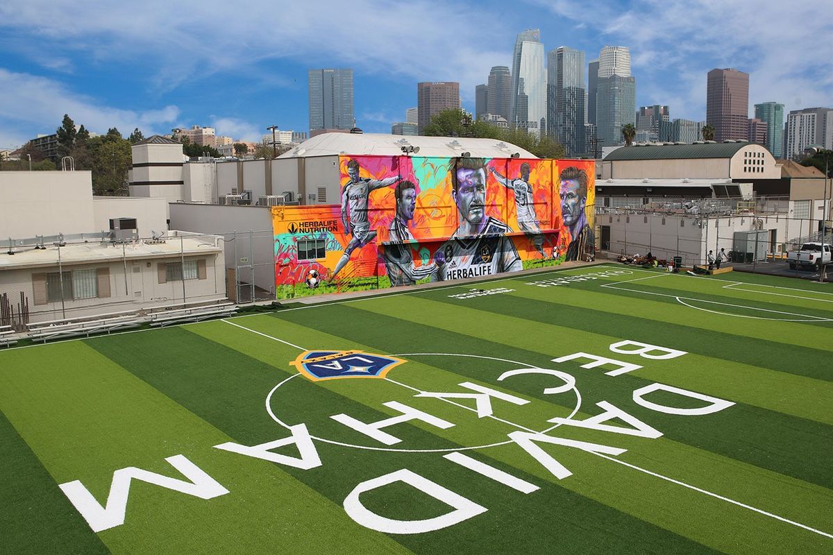 The David Beckham Community Field from an aerial shot features the LA Galaxy logo as well as a colorful mural of David Beckham on the side of the building. 