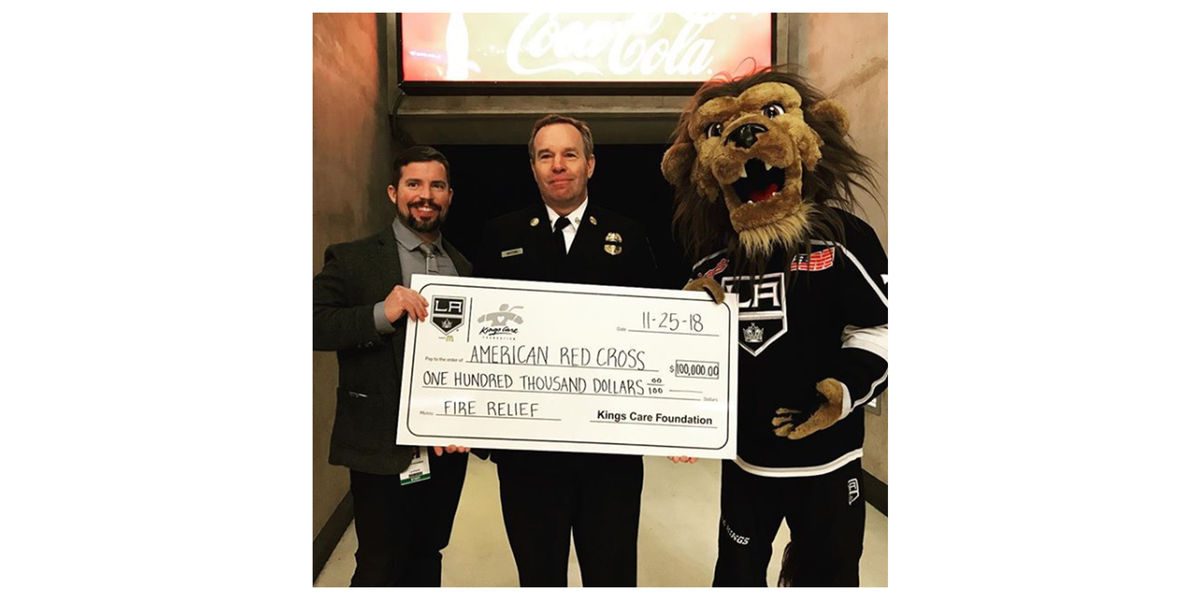 AEG Sports COO Kelly Cheeseman, Chief Deputy Fred Mathis – the Commander of LA City Fire Department’s Administrative Operations Bureau – and LA Kings mascot Bailey hold a $100,000 check for the American Red Cross to be used toward fire relief efforts. 