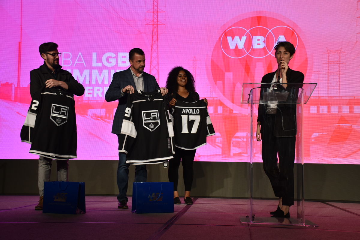 Emma Toshack (right), one of the founders of Nomadica, the business selected to participate in AEG's Inaugural Capacity Building Program, is presented with personalized LA Kings jerseys from members of AEG at the WBA LGBT Economic Impact Summit on March 15, 2019.