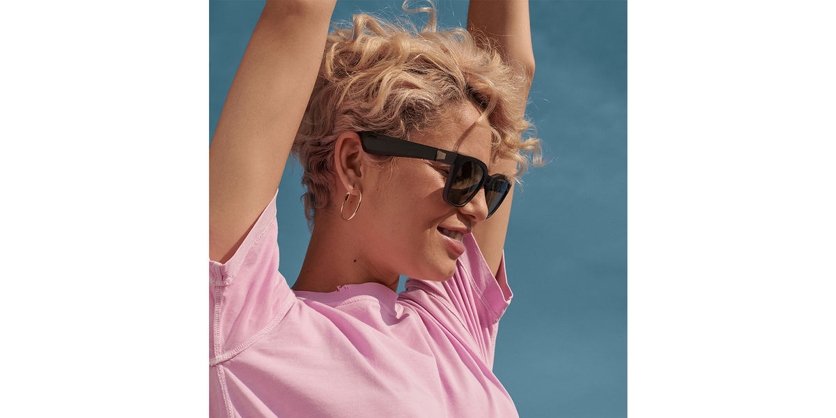 A woman with her arms up, looking in the distance wears the new Bose sunglasses. 