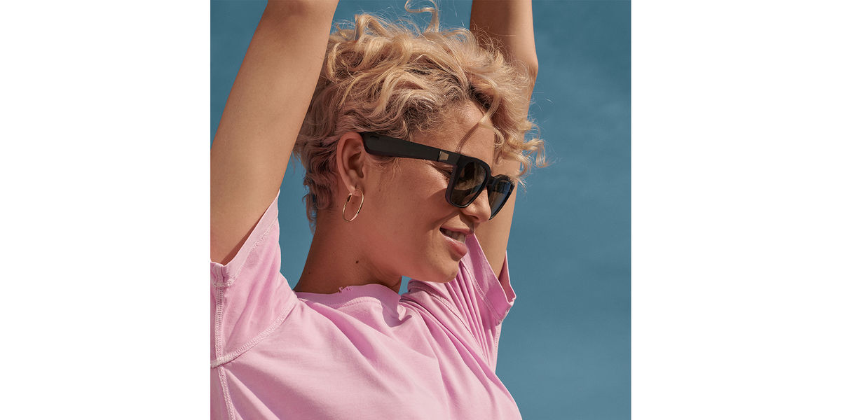 A woman with her arms up, looking in the distance wears the new Bose sunglasses.