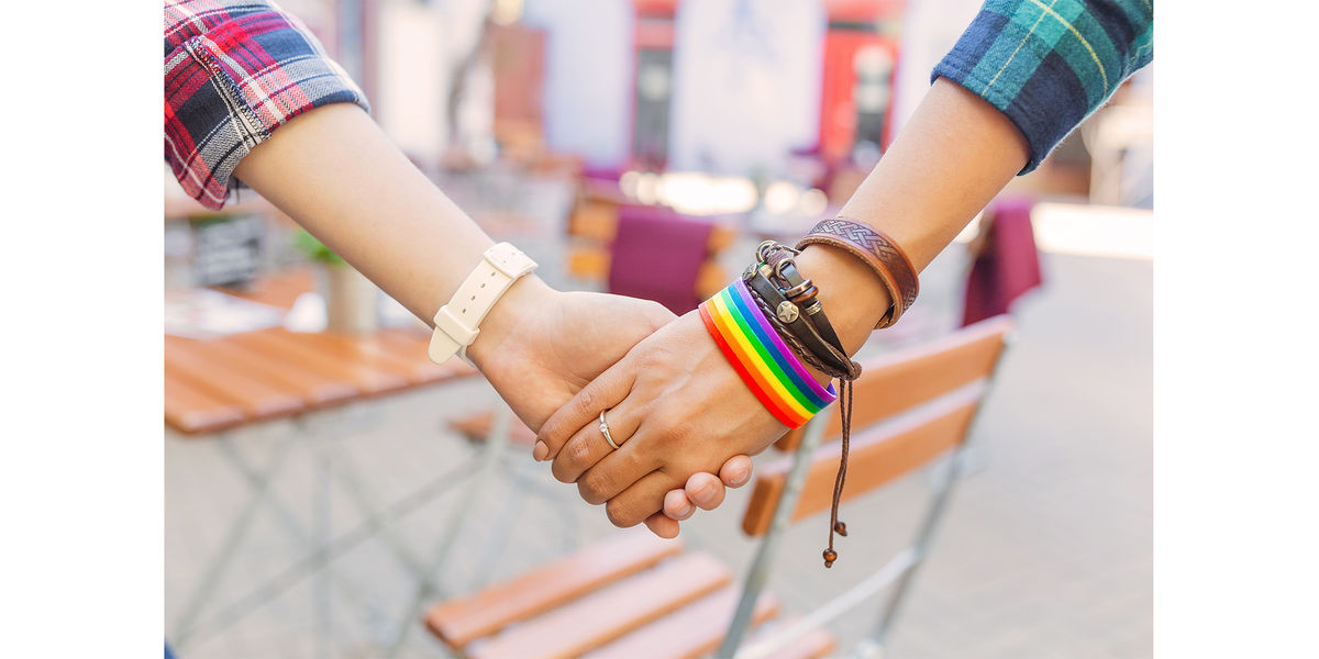 Two women hold hands - one with a Pride rainbow bracelet on.