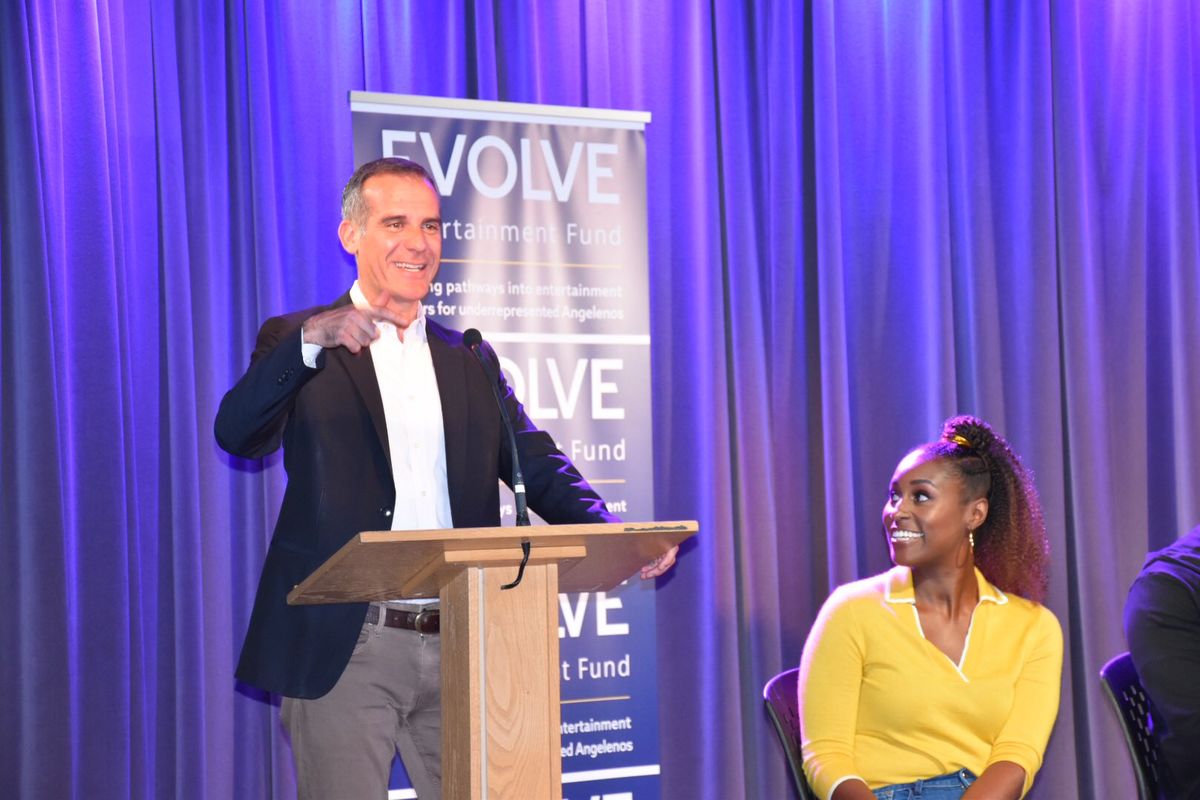 Mayor Eric Garcetti addresses the crowd from a podium as Issa Rae looks to him from stage during the Evolve Entertainment Fund 2019 Summer Kickoff at L.A. LIVE. 