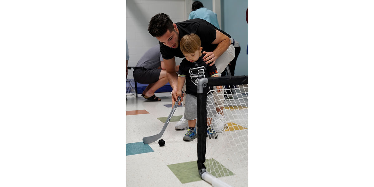 LA Kings prospect Sean Durzi plays ball hockey and shows a young patient how to shoot the ball into the net at the Pediatric Therapy Network in Torrance, Calif. during a team visit on June 27, 2019.
