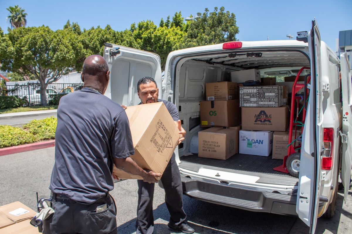 Two men load boxes of donated materials from the Los Angeles Convention Center into a van. 