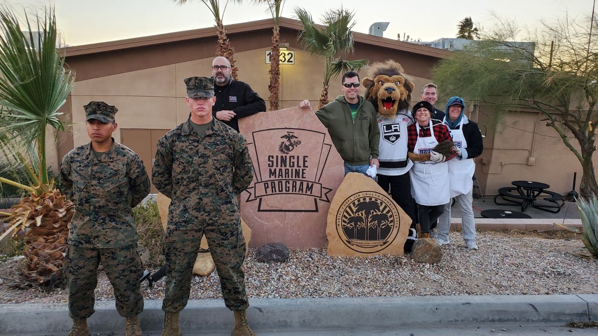 Two marines stand at attention in with LA Kings mascot Bailey and members of the USO during a watch party at the military training facility Twentynine Palms for Marines.