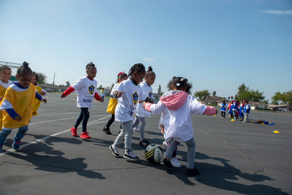 A group of small children run after a soccer ball on the blacktop at school during an LA Galaxy Youth Soccer Clinic hosted by the LA Galaxy Foundation.