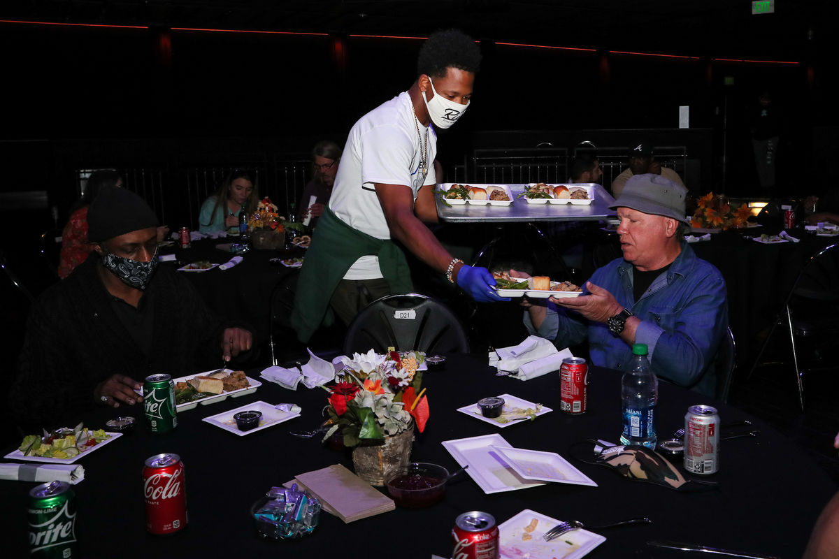 An AEG volunteer hands a tray of food of Thanksgiving favorites to a veteran siting at a table at The Novo in Los Angeles